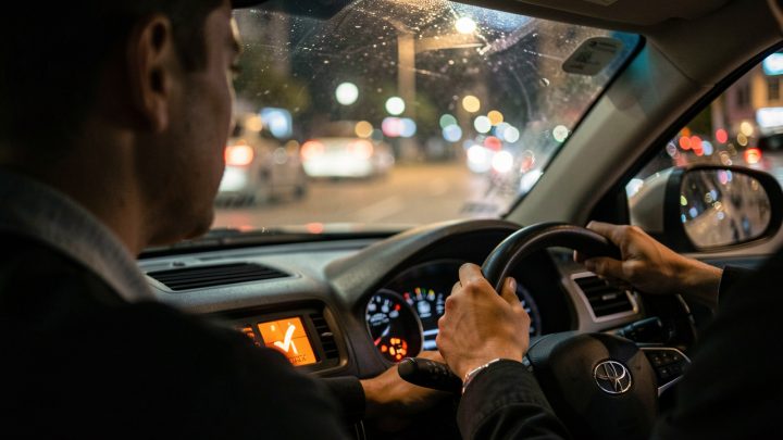 Gros plan du tableau de bord d’une voiture de nuit avec un voyant moteur orange allumé, ambiance urbaine réaliste de conduite et conducteur masculin attentif.