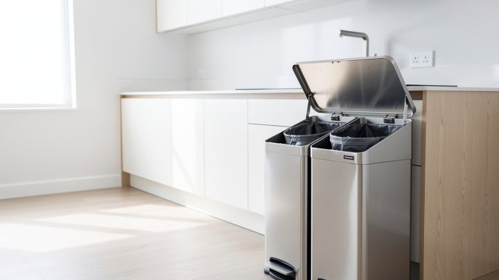 Cuisine contemporaine lumineuse avec une poubelle de tri à deux compartiments en inox près du plan de travail et des sacs de tri discrets.